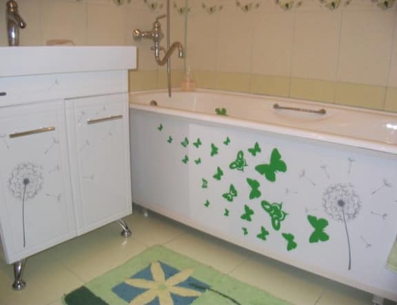 Зеленый коврик и рисунки на экране ванны оживляют однотонное белое помещение