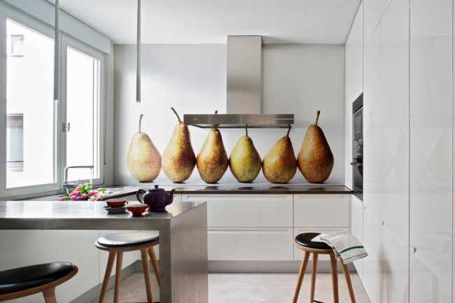 Крупные аппетитные фрукты на стеклянном фартуке в минималистичном белом интерьере кухни
