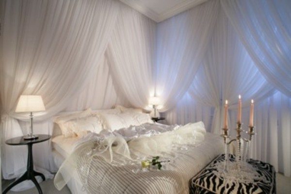 Белая спальня для молодоженов, в которой стены задрапированы легкой тканью.