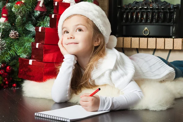 Красивая девушка в шляпе Санта пишет письмо Деду Морозу — стоковое фото