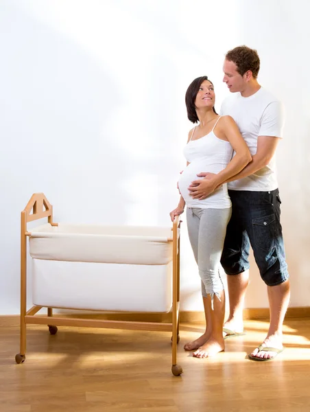 Пара с беременной обниматься с колыбели младенца — стоковое фото
