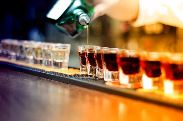 Бармен, заливки крепкий алкогольный напиток в небольшие бокалы на бар, рюмки — стоковое фото