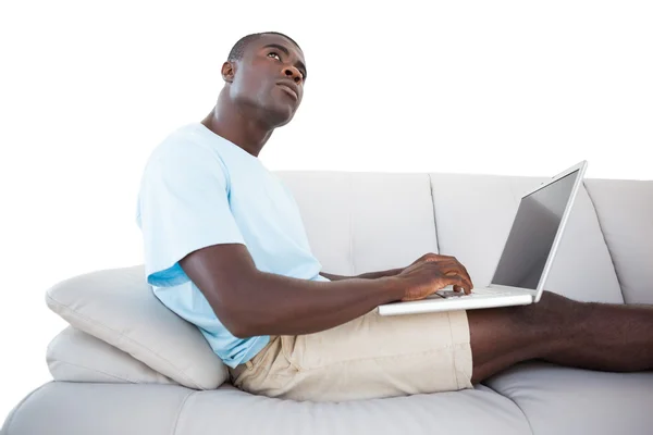 Вдумчивый человек, сидя на диване, с помощью ноутбука — стоковое фото