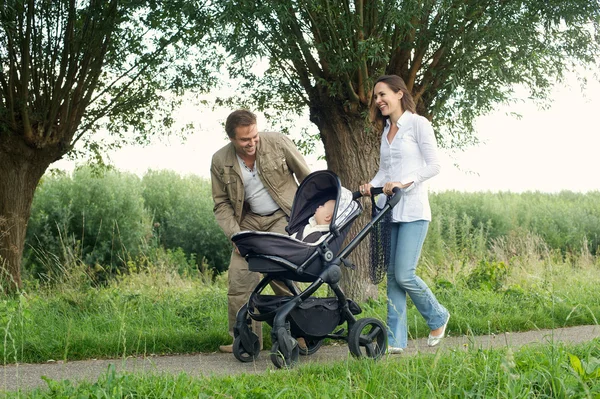 Счастливая мать и отец, ходьбе на открытом воздухе с ребенком в коляске — стоковое фото