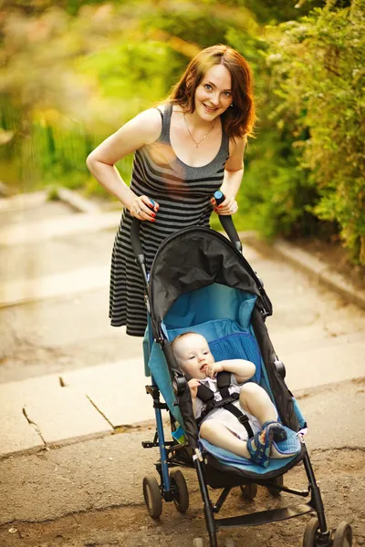 Счастливая молодая мать с ребенком в детской коляске, идущей в парке — стоковое фото
