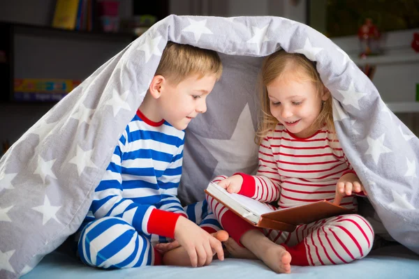 Счастливый братьев и сестер, чтение книги под крышкой — стоковое фото