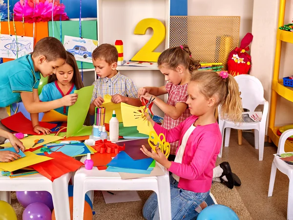 Kids holding colored paper on table in kindergarten . — стоковое фото