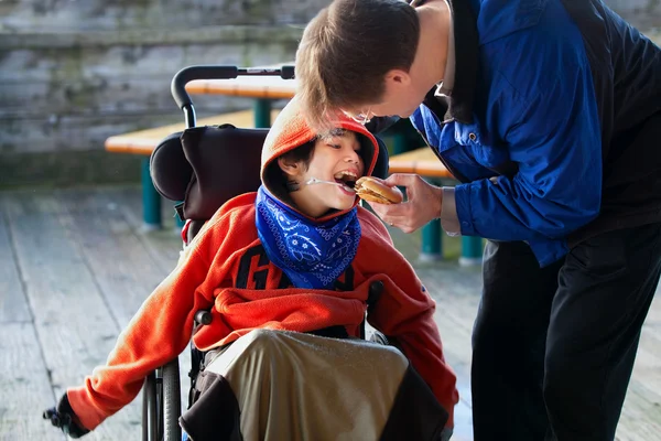 Отец, питающийся, искалечил сына гамбургер в инвалидном кресле. ребенок имеет — стоковое фото