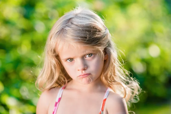 Крупным планом портрет грустно блондинка маленькая девочка с поджатые губы. Солнечный летний день в прекрасном парке — стоковое фото