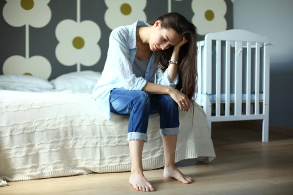 Молодой устал женщина, сидя на кровати рядом детская кроватка — стоковое фото
