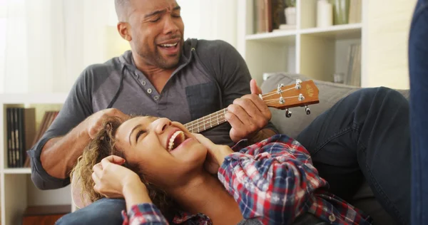 Счастливая темнокожая пара, лежащая на диване с гавайской гитарой — стоковое фото