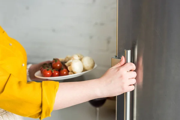Обрезанное Изображение Женщины Открытия Холодильник Держа Тарелку Шампиньонами Томатами Кухне — стоковое фото
