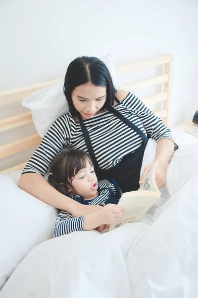 Счастливая любящая семьи молодых азиатских мать преподавания ее дочь для чтения книги История времени кровати — стоковое фото