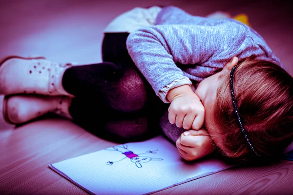 Расстроен маленькая девочка, свернувшись калачиком рядом с ее рисунок — стоковое фото
