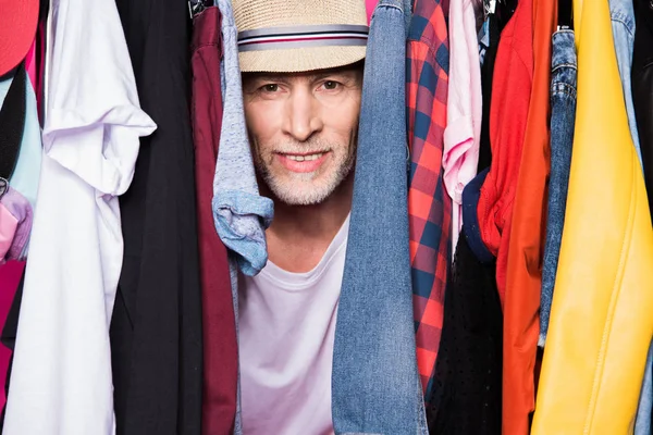 Старший мужчина с разной одеждой на вешалках — стоковое фото
