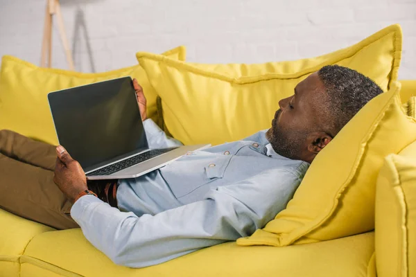 African American Man Using Laptop Blank Screen While Lying Sofa — стоковое фото