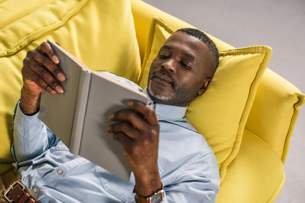 Senior African American Man Lying Sofa Reading Book — стоковое фото