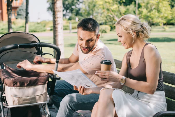 Wife Showing Newspaper Surprised Husband Bench Baby Carriage Park — стоковое фото