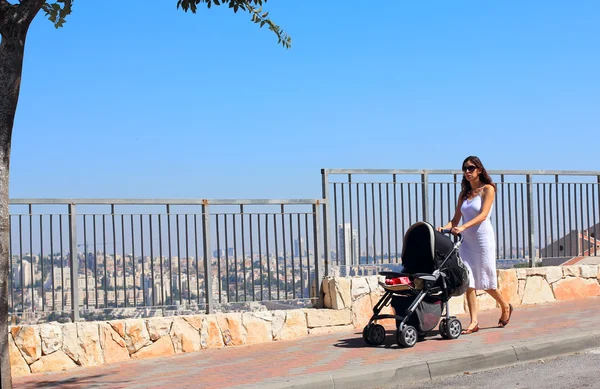 Молодая мать, прогулки с коляской на фоне большой — стоковое фото