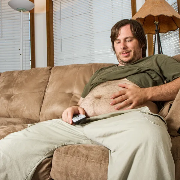 Тяжелые задать человек на диване, любуясь его желудок — стоковое фото